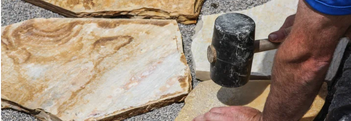 Person verlegt Steinplatte mit Gummihammer